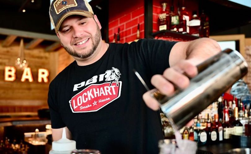 A smiling bartender pours a drink, just one of the many great careers our entertainment districts have to offer!